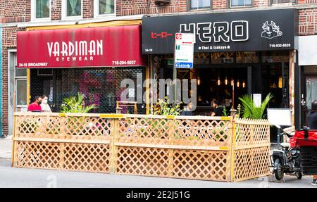 Astoria, New York, USA - 30 luglio 2020: Persone che mangiano ai tavoli posti in città strada circondata da barricata di legno in Astoria Queens a causa di New Yor Foto Stock
