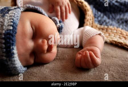 Bambino bambino dolce neonato con guance chubby dormire a letto coperto da plaid in caldo cappello di maglia blu durante il giorno Foto Stock