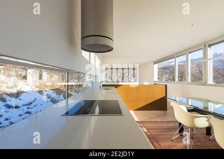 Cucina con sala da pranzo di un appartamento accogliente e moderno.ampia finestra con vista su un cielo blu montagne alla foresta. Foto Stock