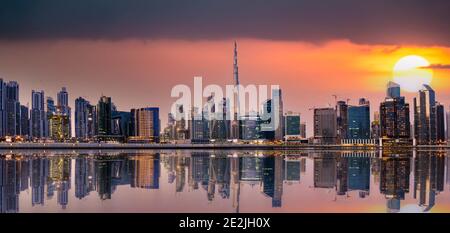 Vista panoramica dello skyline di Dubai al tramonto con edifici e grattacieli riflessi sul fiume Singapore che scorre in primo piano. Dubai, Emirati Arabi Uniti Foto Stock