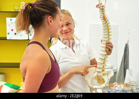 Paziente giovane donna alla consultazione di fisioterapia, fisioterapista che spiega le ossa posteriori sul modello della spina dorsale Foto Stock