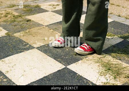 Donna in sneaker rosse e pantaloni verdi in piedi fuori grandi quadratini a scacchi bianchi e neri pieni di erba tagliata e fieno Foto Stock