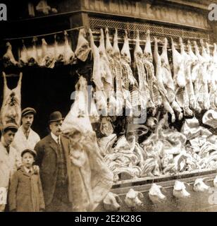 Una prima fotografia di un macellaio tradizionale a Whitby, nel Nord Yorkshire, Inghilterra. Il proprietario del negozio, la sua famiglia e il personale posa alla porta, whils la finestra contiene una massiccia esposizione di carne (compresa una fila di teste di maiale) probabilmente al tempo di Natale. Foto Stock