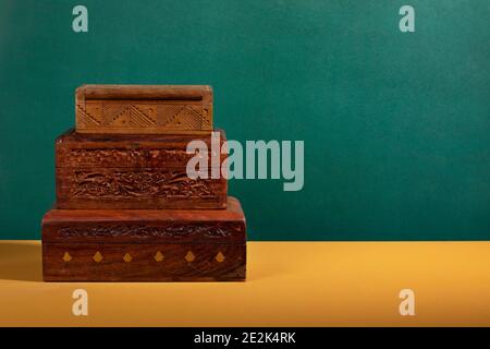 Vecchie scatole di legno intagliate a mano d'epoca in colori marrone scuro accatastate su una superficie gialla con uno sfondo verde. Una collezione di autentico legno fatto a mano Foto Stock