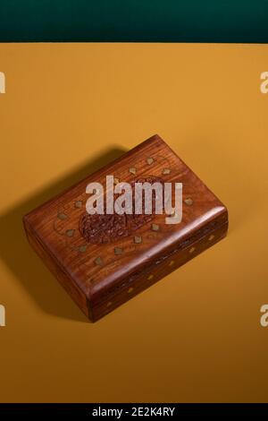 Antica scatola di legno intagliata a mano d'epoca in un colore marrone scuro con dettagli dorati su una superficie gialla con sfondo verde. Un antico e autentico fatto a mano Foto Stock
