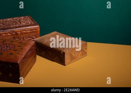 Vecchie scatole di legno intagliate a mano d'epoca in colori marrone scuro su una superficie gialla con uno sfondo verde. Una collezione di autentici manufatti in legno intagliato tr Foto Stock