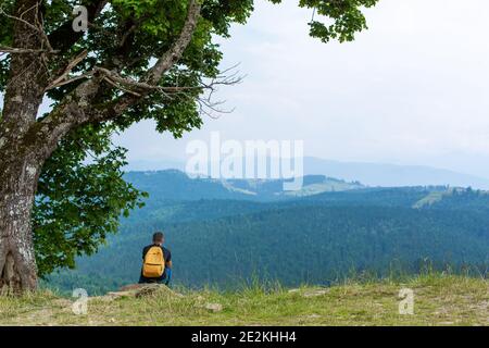 Solo ragazzo seduto sulla scogliera e godere di un tranquillo paesaggio verde montagne. Tranquillità e relax. Foto Stock