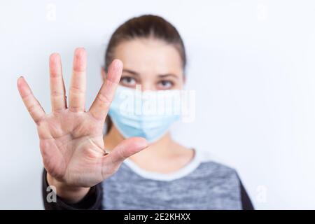 Giovane bella donna in maschera medica mostra stop con la mano, su uno sfondo bianco. Foto Stock