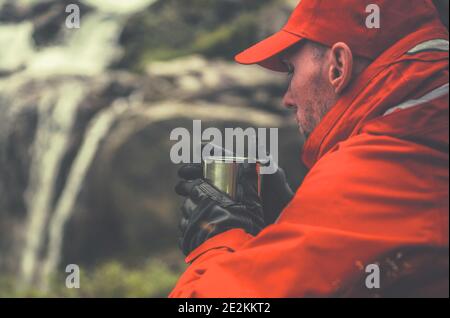 Gli uomini caucasici nei suoi anni 30 bevono tè caldo dalla sua Metal Cup mentre si brevi pause sulla testa di trincea alpina. Riscaldamento escursionista. Foto Stock