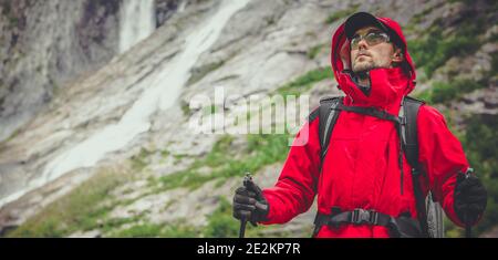 Sport all'aperto e tema ricreativo. Hiker caucasico negli anni '30 indossando Raincoat rosso e occhiali Safety Sport sulla Scenic Alpine Trailhead. Rocce e. Foto Stock