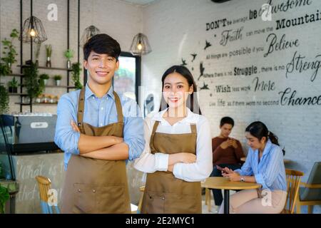 Coppia asiatica barista o proprietario piccola impresa in grembiule cercando A macchina fotografica pronto per offrire il servizio caffè al moderno caffetteria Foto Stock