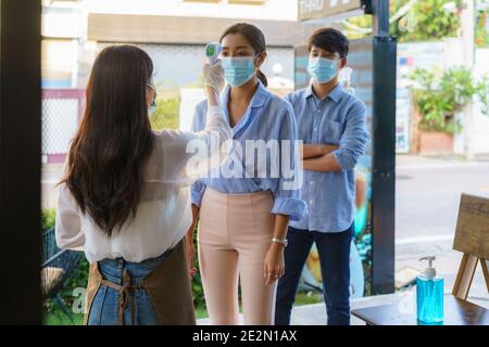 Donna asiatica impiegato caffè prendere temperatura asiatica donna con faccia maschera prima di andare al ristorante o caffè per nuovo stile di vita normale coronavirus cov Foto Stock