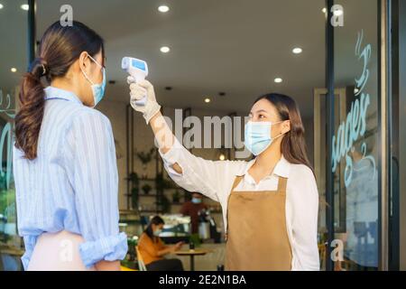 Donna asiatica impiegato caffè prendere temperatura asiatica donna con faccia maschera prima di andare al ristorante o caffè per nuovo stile di vita normale coronavirus cov Foto Stock