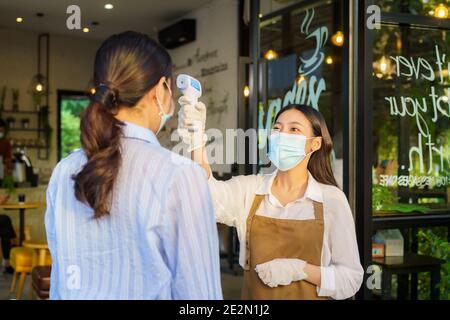 Donna asiatica impiegato caffè prendere temperatura asiatica donna con faccia maschera prima di andare al ristorante o caffè per nuovo stile di vita normale coronavirus cov Foto Stock