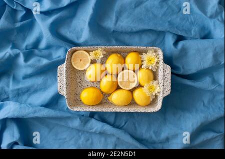 Sistemazione estiva con limoni e fiori gialli in un bagno d'acqua su un telo da spiaggia di lino blu. Sfondo astratto. Foto Stock