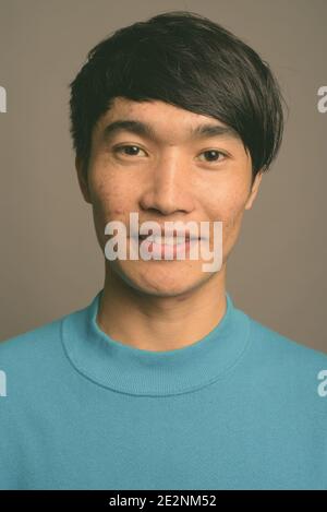 Giovane uomo asiatico che indossa un maglione blu contro uno sfondo grigio Foto Stock