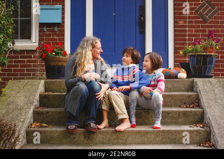 Una mamma sorridente si siede con i suoi due figli davanti stoop di casa Foto Stock