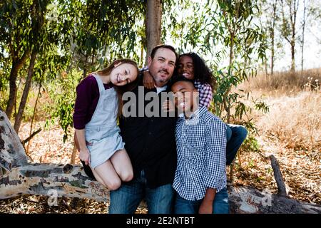 Papà e bambini che abbracciano e sorridono per la fotocamera al Park A Chula Vista Foto Stock
