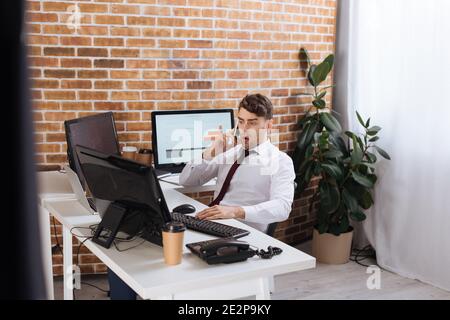 Uomo d'affari stupito che parla su smartphone mentre controlla le scorte di forex sopra computer Foto Stock