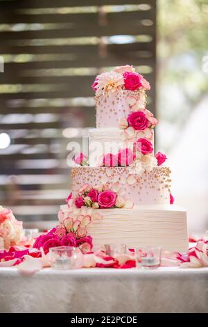 Torta di nozze a quattro livelli con glassa bianca decorata con rose rosa su un tavolo bianco per una cerimonia nuziale Foto Stock