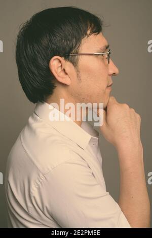 Giovani asiatici nerd uomo che indossa occhiali contro uno sfondo grigio Foto Stock