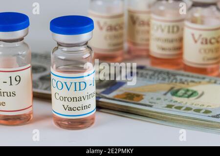 Flaconi di vaccino contro il coronavirus SARS-COV-2 e banconote in dollari americani la pandemia sulla maschera chirurgica protettiva Foto Stock