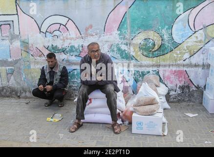 Gaza, Palestina. 14 gennaio 2021. I palestinesi attendono di ricevere forniture alimentari in un centro di distribuzione degli aiuti nel campo profughi di al-Shati, nella città occidentale di Gaza. I rifugiati palestinesi nella striscia di Gaza hanno criticato la decisione delle Nazioni Unite di tagliare gli aiuti e i servizi loro forniti. La maggior parte dei residenti di Gaza sono rifugiati che sono stati espulsi dalle loro città e villaggi quando il regime israeliano è stato istituito nel 1948. Credit: SOPA Images Limited/Alamy Live News Foto Stock