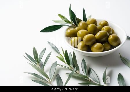 Olive salate e rami d'oliva posti su sfondo bianco con spazio per la copia Foto Stock