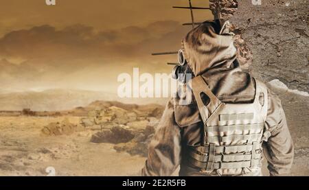 Foto di uno stalker in giacca, gilet corazzato in vista posteriore in maschera a gas sovietica con filtro su sfondo desertico apocalittico distrutto. Foto Stock