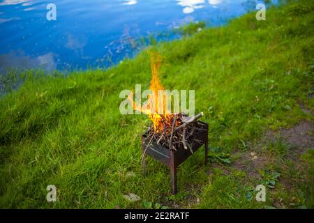 Un piccolo braciere pieghevole portatile riempito di legno in fiamme Foto Stock