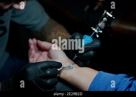 Una vista ravvicinata di una donna che riceve la lettera "s" con un cuore tatuato all'interno del polso. Foto Stock