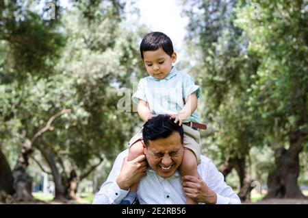 L uomo dando giovane ragazzo piggyback ride sorride all'aperto Foto Stock