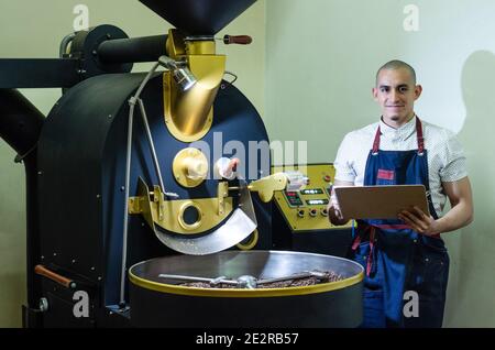 Le mani dell'uomo arrostire i chicchi di caffè aromatico su un moderno macchina utilizzata per tostare i fagioli Foto Stock