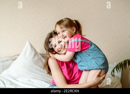 Felici i bambini che si divertono con i cuscini su bed.children giocare in camera da letto. Due sorelle. Adolescente e bambina ridono, abbraccio e bacio. Foto Stock