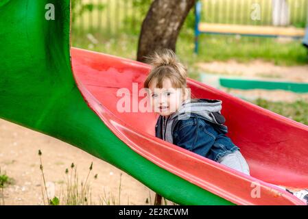 Carino ragazza allegra bambino sul parco giochi. Estate nel parco. Semi su un altalena. Giochi per bambini, corse e salti. Infanzia spensierata. Foto Stock