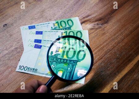 Ingrandimento con una lente di ingrandimento del valore di uno delle centinaia di euro di bollette che sono su un legno superficie Foto Stock