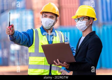 Capo magazzino logistico asiatico maschile con lavoratore utilizzando laptop che controlla la pianificazione elenco e la strategia di contenitori scatole da carico nave. Industr Foto Stock