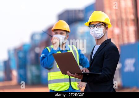 Capo magazzino logistico asiatico maschile con lavoratore utilizzando laptop che controlla la pianificazione elenco e la strategia di contenitori scatole da carico nave. Industr Foto Stock