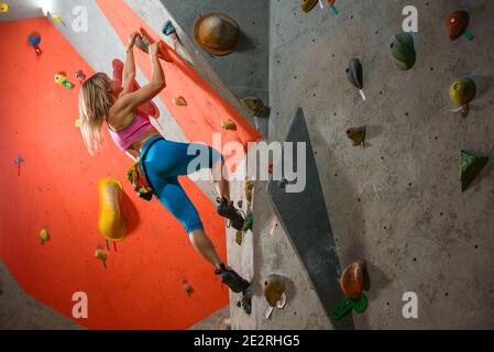 Donna arrampicatrice pratica roccia-arrampicata nella palestra Bouldering. Concetto di sport estremo e arrampicata in interni Foto Stock