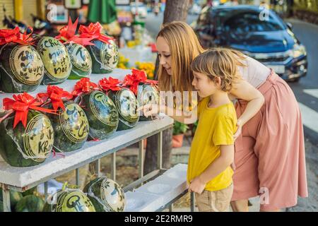 I turisti di mamma e figlio guardano i cocomeri con l'incisione festosa alla vigilia di Tet. Tet è Capodanno lunare e celebrato durante quattro giorni in Vietnam Foto Stock