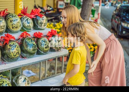 I turisti di mamma e figlio guardano i cocomeri con l'incisione festosa alla vigilia di Tet. Tet è Capodanno lunare e celebrato durante quattro giorni in Vietnam Foto Stock