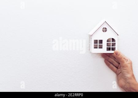 Mano di una donna che tiene un modello di casa di legno bianco. Agente immobiliare offrire casa, assicurazione sulla proprietà e sicurezza. Acquistare e affittare casa concetto. Bianco b Foto Stock