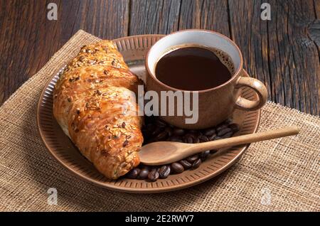 Tazza di caffè caldo e croissant con semi di sesamo piatto su tavolo di legno scuro Foto Stock