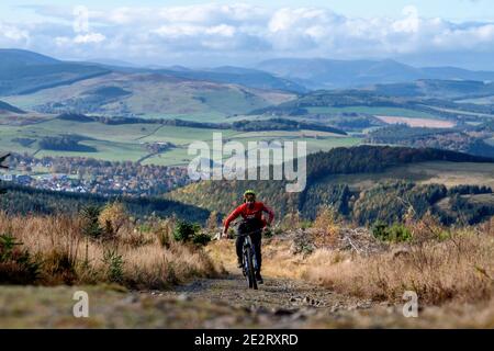 Un uomo guida una mountain bike elettrica in salita lungo una strada ghiaiosa nelle colline sopra la città di Peebles nei confini scozzesi. EBike Scotland. Foto Stock