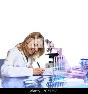 Giovane scienziata femminile o tecnologia scrive rapporto o giornale di laboratorio in laboratorio moderno con microscopio, provette di vetro con campioni in provette, questa immagine è Foto Stock