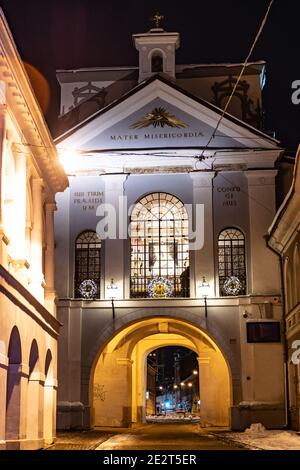 La porta dell'alba o Aurora a Vilnius, la cappella di nostra Signora della porta dell'alba è nel mezzo dietro la finestra di vetro, vista notturna con neve, vert Foto Stock