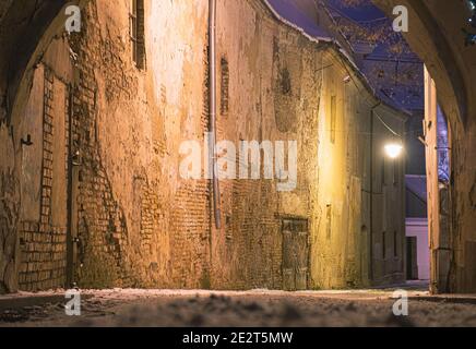 Bella strada stretta della Città Vecchia di Vilnius, vista serale o notturna con vecchi edifici e lampione in inverno con neve Foto Stock