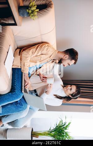 Tempo con la famiglia in quarantena. Bella giovane donna in abiti bianchi si preoccupa di suo marito o ragazzo portandolo gustoso tè caldo. Uomo professionale Foto Stock