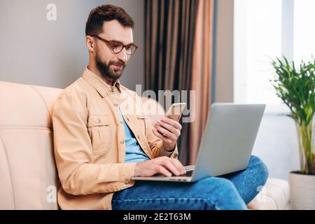 Concetto di lavoro remoto. Un giovane professionista intelligente in occhiali può contenere computer portatile e smartphone. Designer, programmatore o contabile che lavora da casa Foto Stock