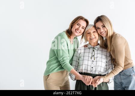 tre generazioni di donne felici che guardano la macchina fotografica e la tenuta mani isolate su bianco Foto Stock